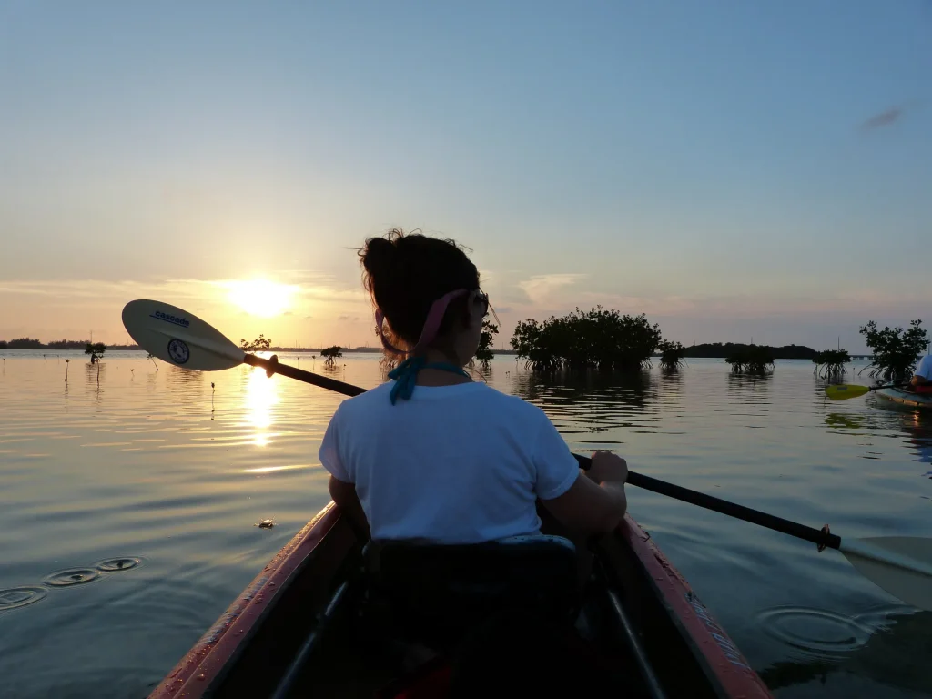 Person kayaking at sunset on calm water with scenic view