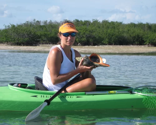 Woman kayaking and holding a large seashell in tropical water