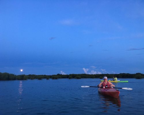 Two people kayaking on calm lake under evening sky