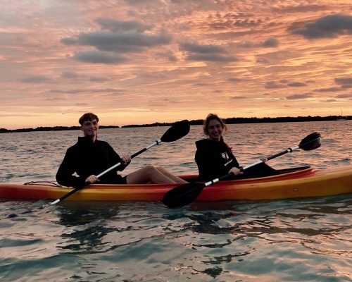 Two people kayaking on a serene lake during a stunning sunset