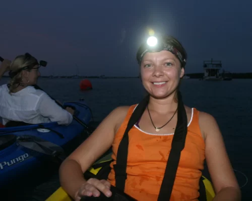 Woman kayaking at night with headlamp on calm water
